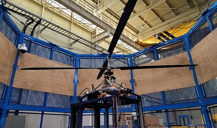 실내에 설치된 파란색 금속 울타리 안에서 대형 헬기 로터가 테스트를 받고 있는 모습