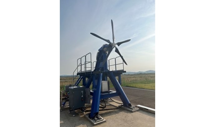 파란색 철제 구조물 위에 수직으로 장착된 5엽 프로펠러를 야외에서 테스트하는 모습. 계기장비와 안전 난간이 설치되어 있으며 멀리 산과 초원이 보임.